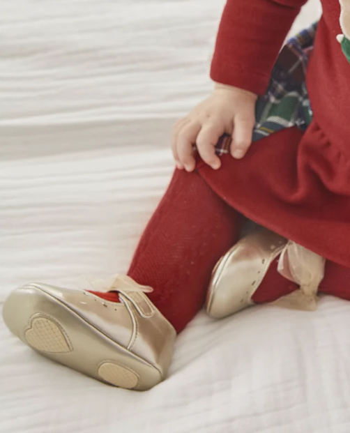 Child's legs wearing red pants and gold shoes on a white surface